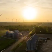 Aerial view of wind turbines and grain silos at sunset in a rural setting, highlighting clean energy and agricultural infrastructure.