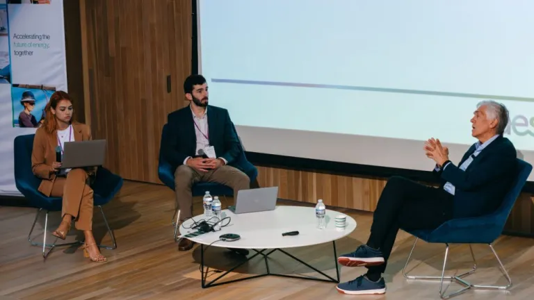Panel discussion with three business professionals seated in modern chairs on stage with AES branding and presentation screen visible