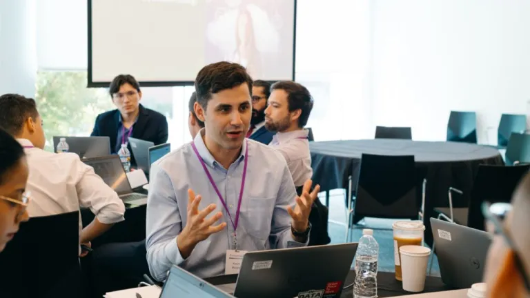 Professional man gesturing while speaking at conference table with laptop and colleagues in background during business meeting