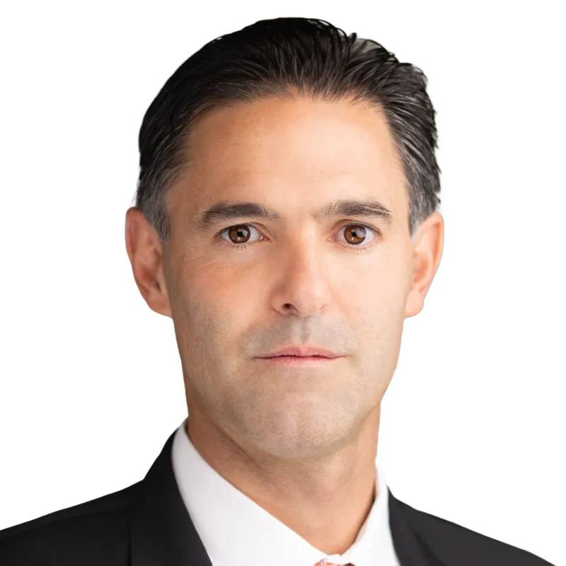 Professional headshot of AES CCO Ricardo Manuel Falu in a black suit, white shirt, and red tie, suitable for corporate profiles or business presentations.