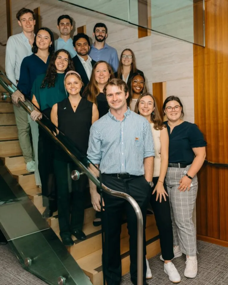 Young professionals group photo on modern office staircase with glass railings and wooden paneling in contemporary corporate building