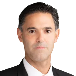 Professional headshot of AES CCO Ricardo Manuel Falu in a black suit, white shirt, and red tie, suitable for corporate profiles or business presentations.