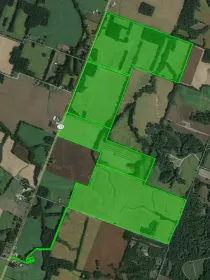 Aerial view of a rural area with fields and forests. A large, irregularly shaped area is outlined and shaded in bright green, indicating a specific land plot. A road labeled '725' runs vertically through the left side of the image, with scattered buildings and patches of trees visible throughout the landscape.