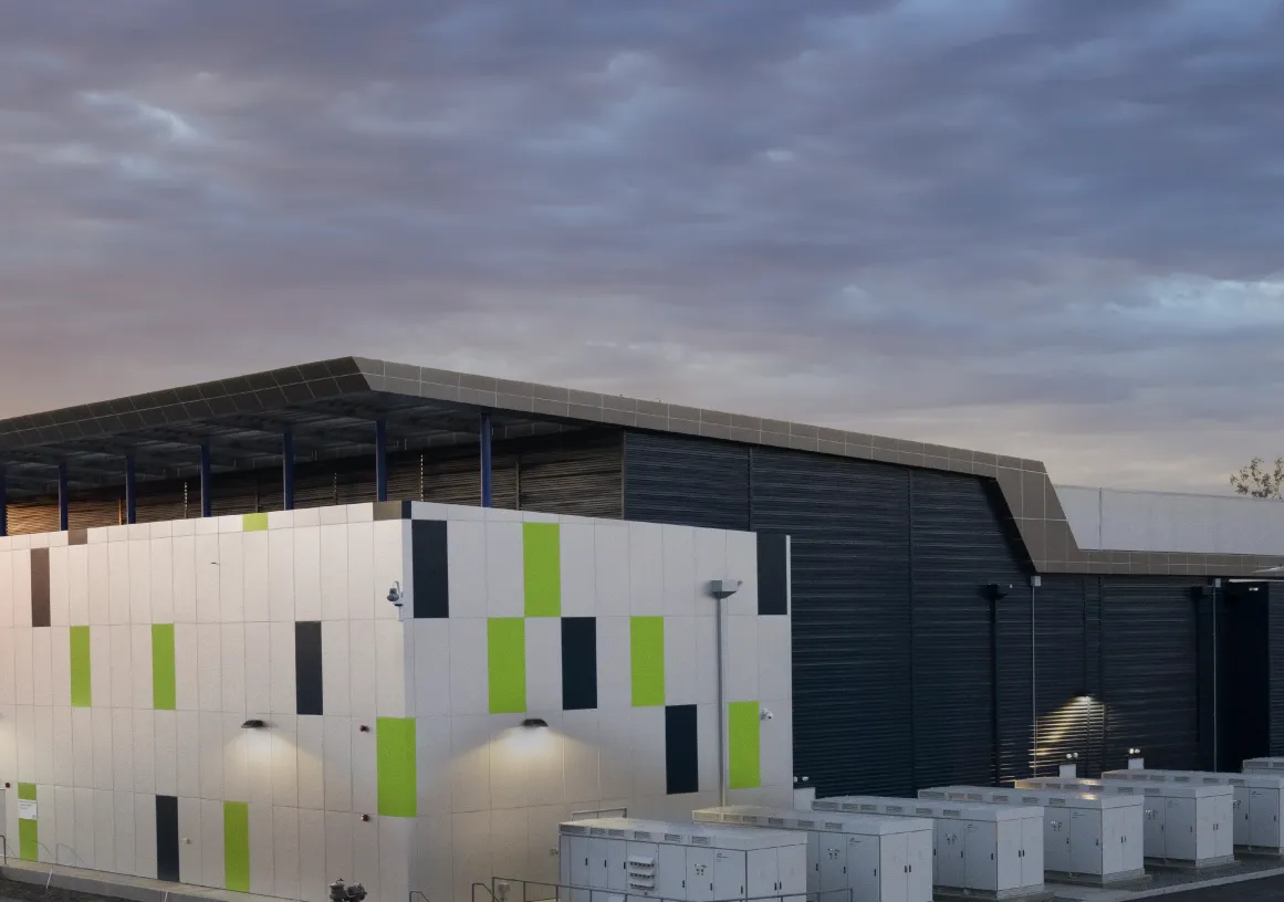 Modern industrial building with colorful geometric panels, surrounded by utility boxes, under a cloudy sky at sunset.