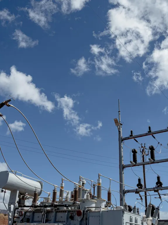 An outdoor electrical substation with transformers and interconnected wires under a blue sky with scattered clouds.