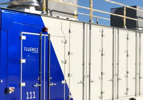 A large industrial container with a blue and white design labeled 'Fluence' and the number '111'. It has multiple doors and is situated outdoors under a clear blue sky.