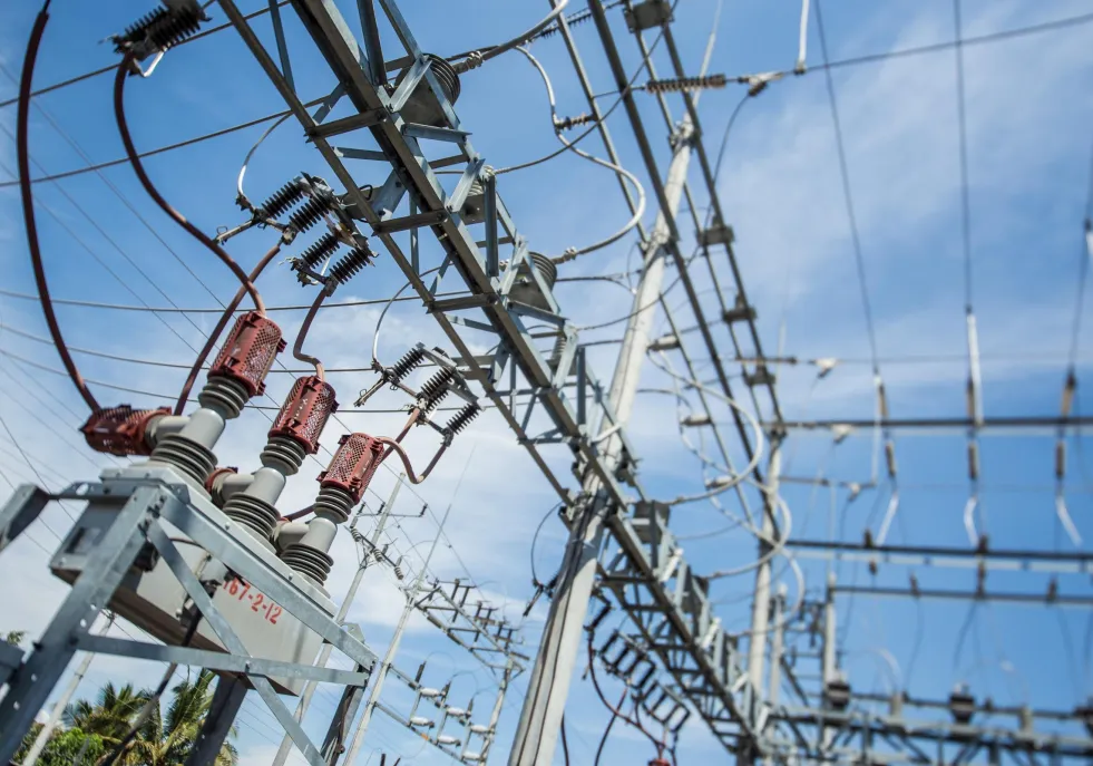 Close-up view of electrical substation equipment with red insulators and metal structures against a blue sky.