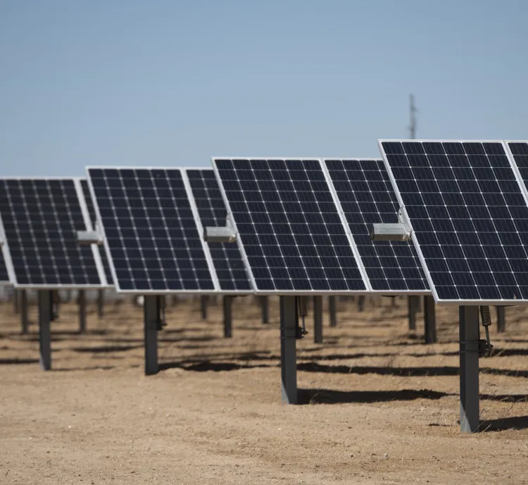 Rows of solar panels installed on a dry, sandy ground under a clear blue sky.