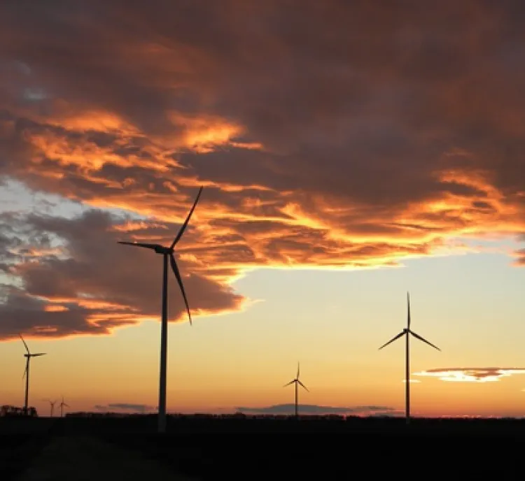 Wind turbines silhouetted against a dramatic sunset sky with orange and purple clouds.