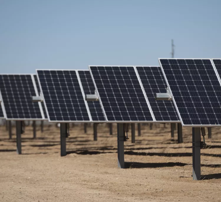 Rows of solar panels installed in a desert landscape under a clear blue sky, mounted on metal supports.