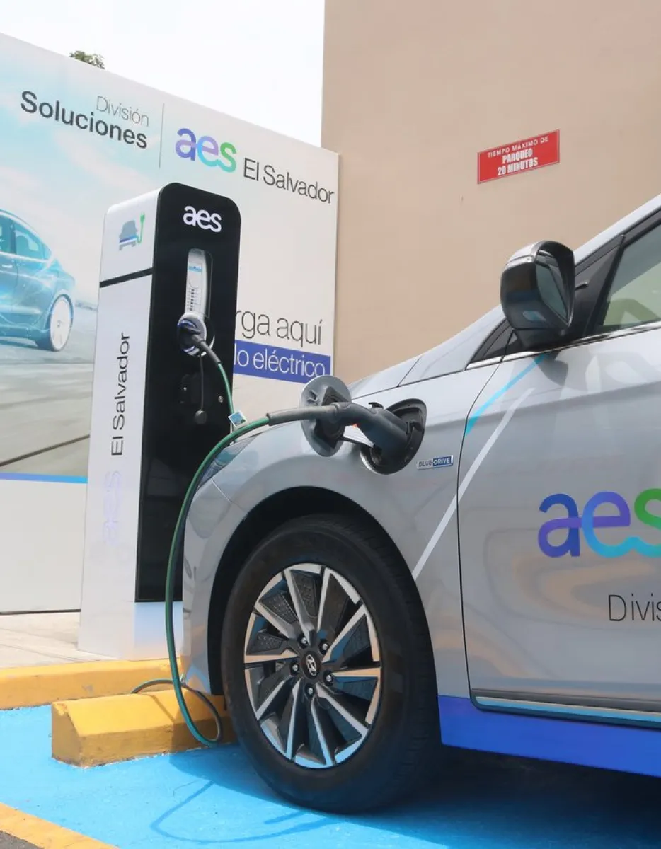 An electric car charges at an AES El Salvador station. Both the car and charger display the AES El Salvador logo and branding