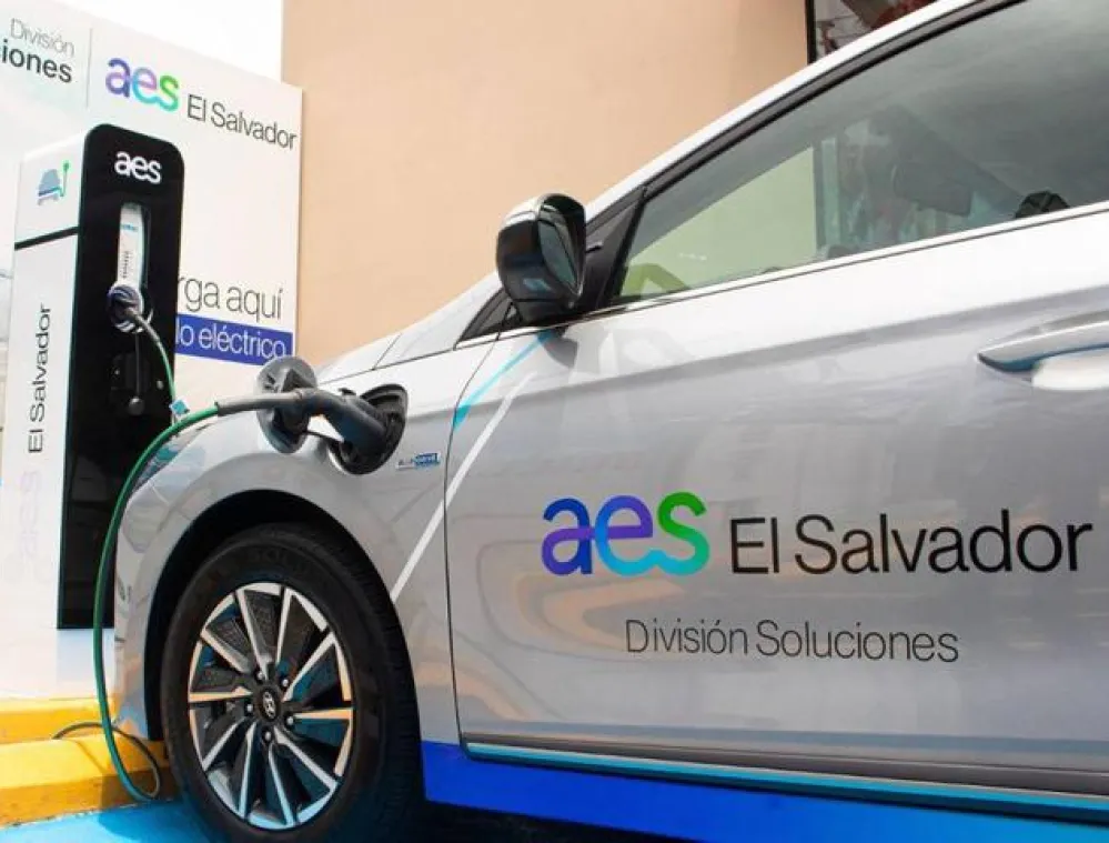 Electric car charging at an AES El Salvador station with branding visible on the vehicle and charging unit.