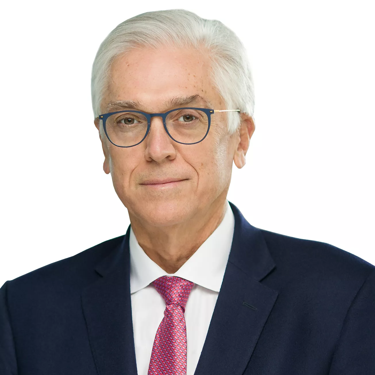 A man with white hair and glasses is wearing a dark suit, white shirt, and red tie, posing against a white background.