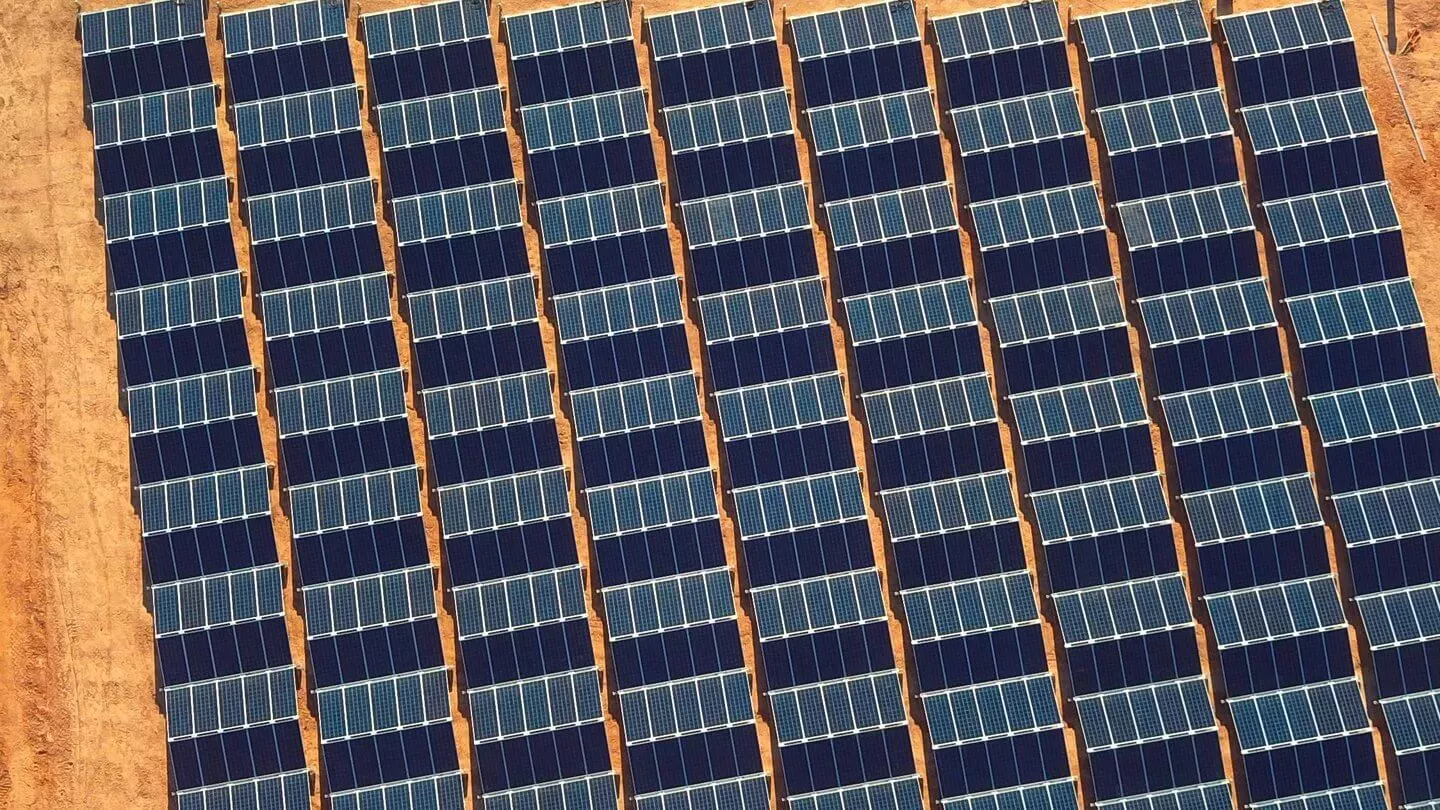 Aerial view of multiple rows of solar panels installed on a sandy terrain, capturing sunlight for energy production.