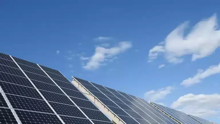 Solar panels angled towards a clear blue sky with a few clouds.